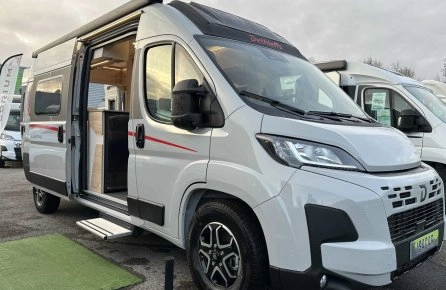 Camping-car Dethleffs blanc avec porte latérale ouverte sur un parking.