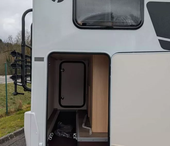 Compartiment de rangement ouvert à l'arrière d'un camping-car sous ciel nuageux