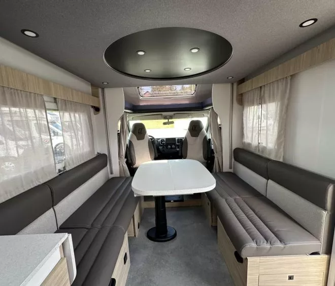 Intérieur spacieux d'un camping-car moderne avec banquettes et table centrale.