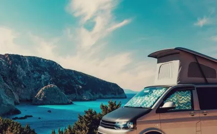 Van aménagé avec toit relevable face à une mer turquoise et falaises
