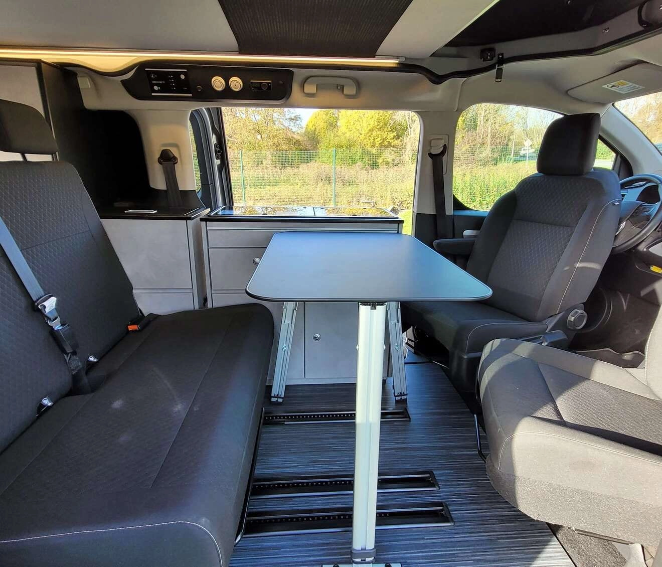 Intérieur d'un van aménagé avec table et sièges, vue sur l'extérieur