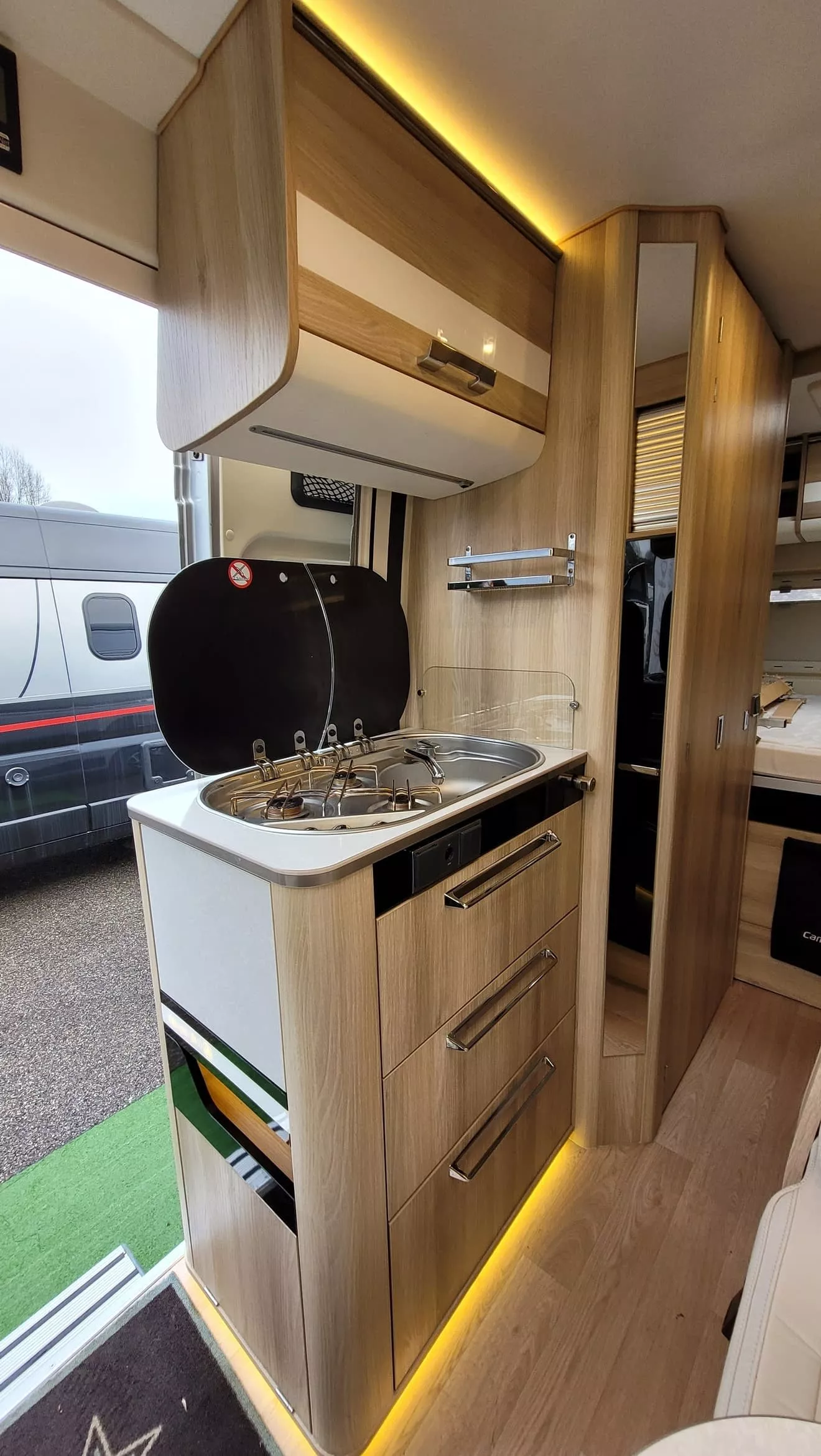 Cuisine compacte en bois dans un camping-car moderne avec plaques de cuisson et rangements.