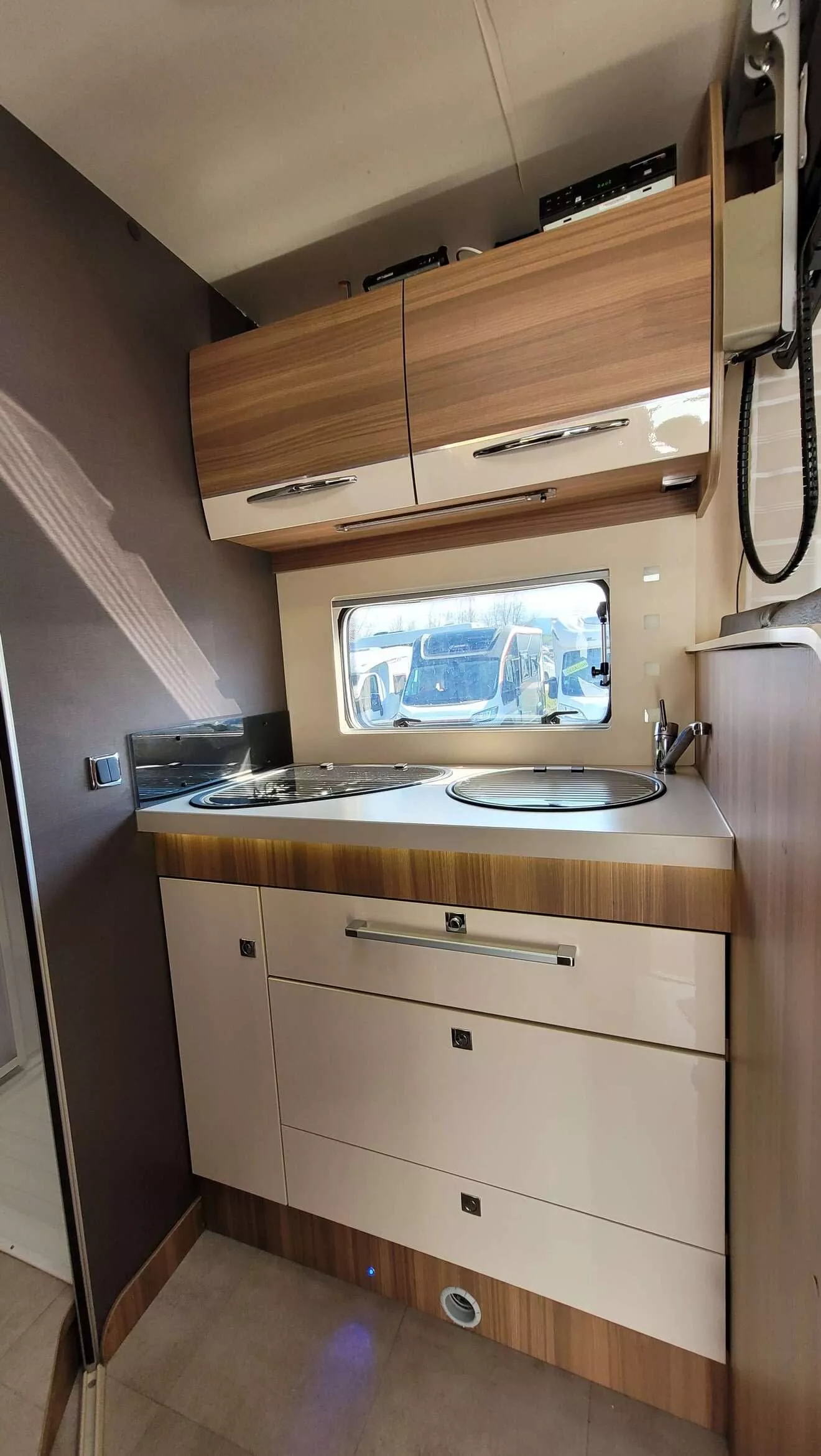 Cuisine compacte de camping-car avec placards en bois et fenêtre.