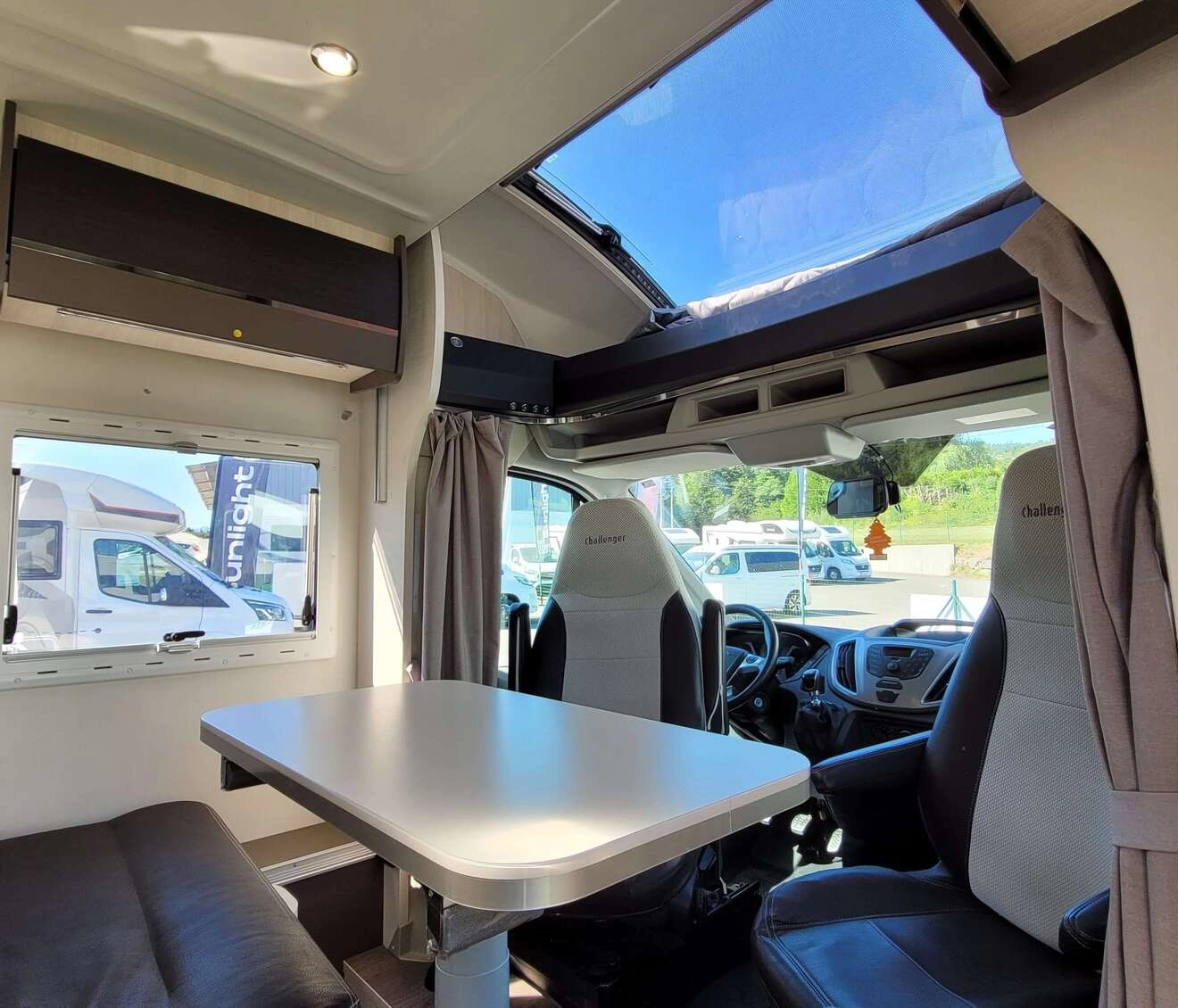 Intérieur d'un camping-car avec table et sièges, vue sur l'extérieur ensoleillé