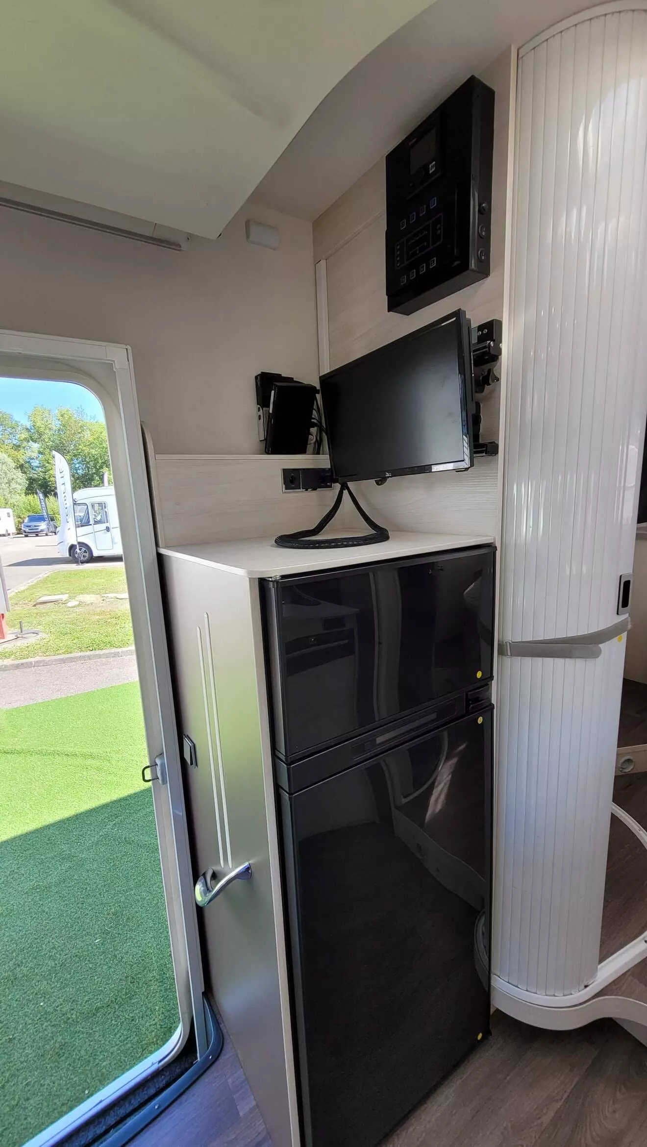 Intérieur d'un camping-car avec réfrigérateur, écran et panneau de contrôle.