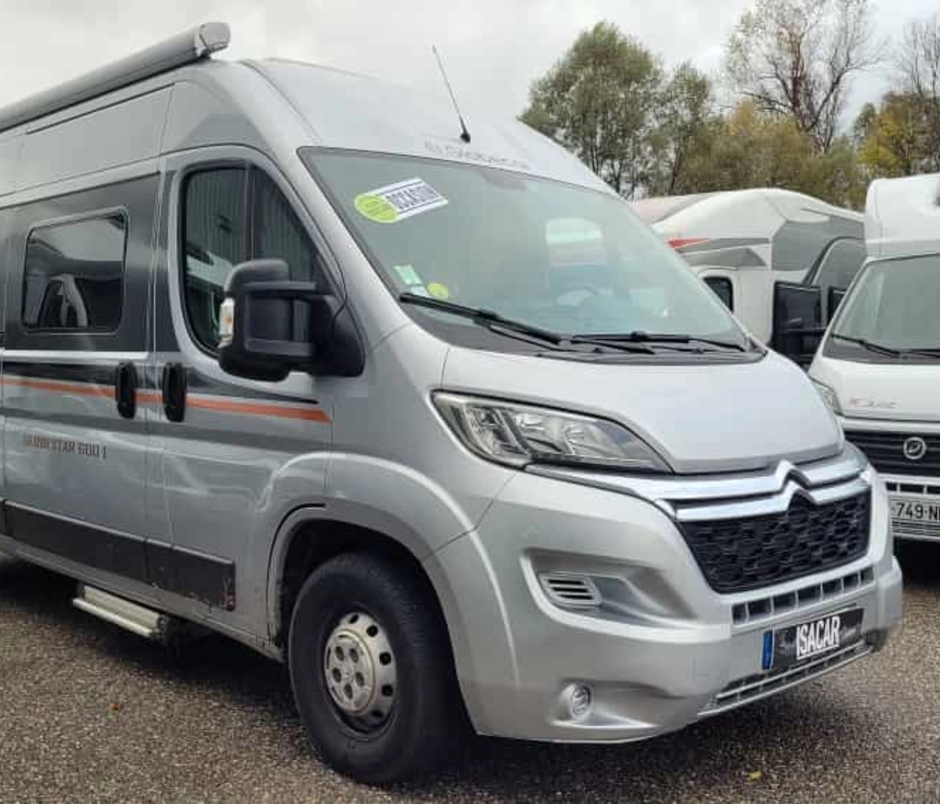 Camping-car Citroën gris stationné sur un parking avec d'autres véhicules similaires.