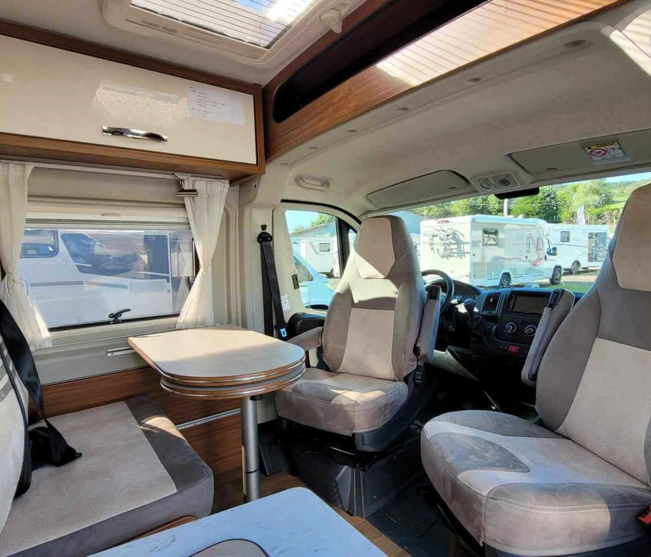 Intérieur d'un camping-car avec sièges et table, vue sur l'extérieur.