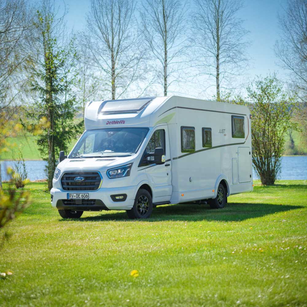 Camping-car Dethleffs garé sur pelouse près d'un lac, arbres en arrière-plan