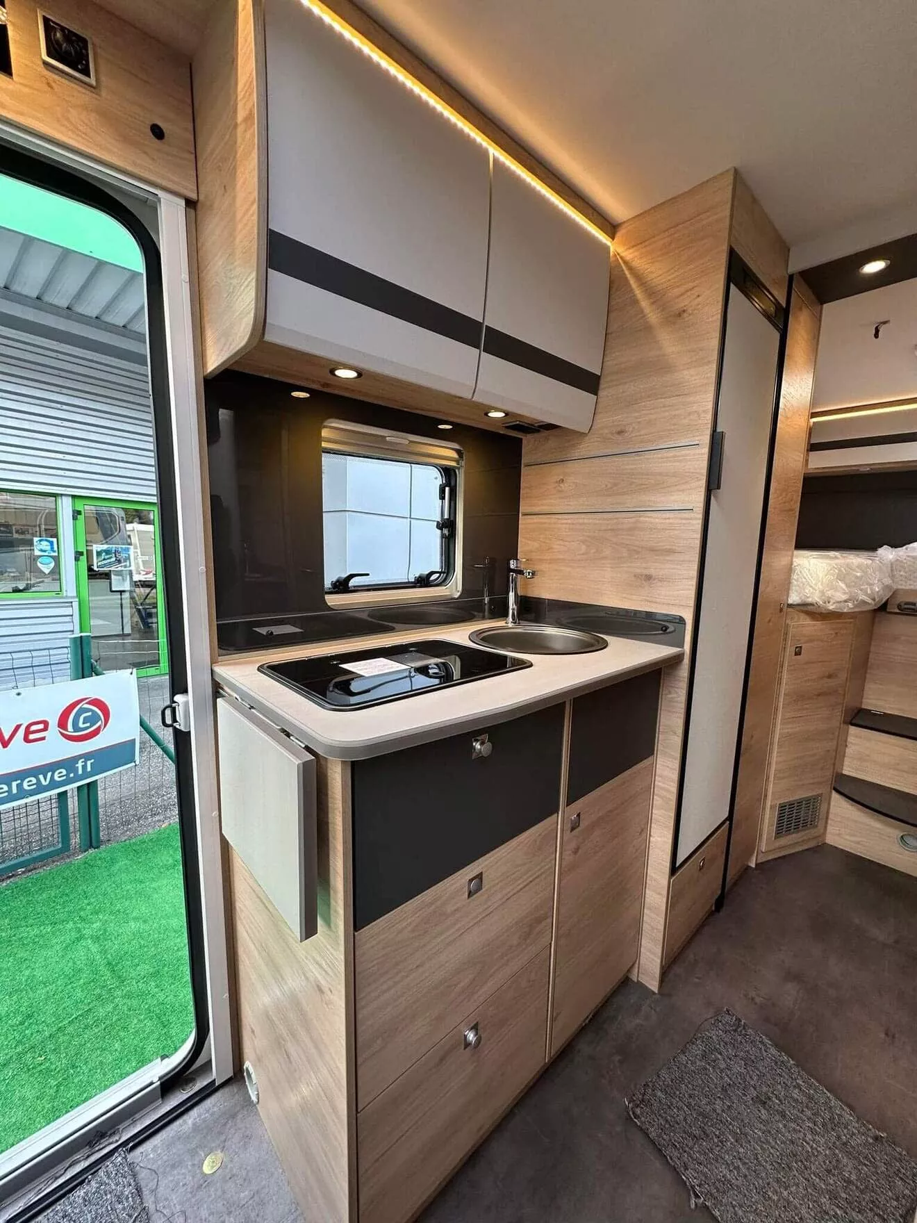 Cuisine moderne d'un camping-car avec évier, plaques de cuisson et rangements en bois clair.