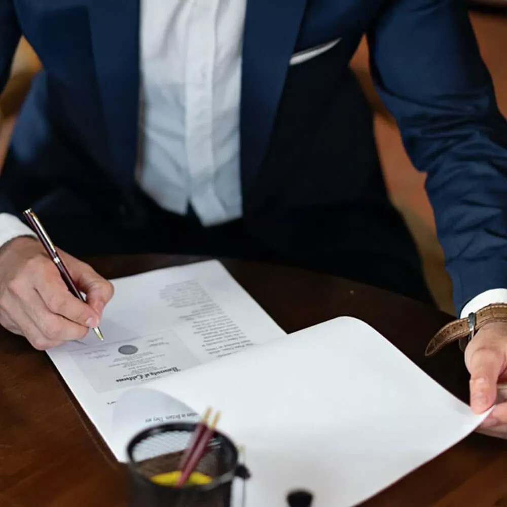 Personne en costume signant un document sur une table en bois