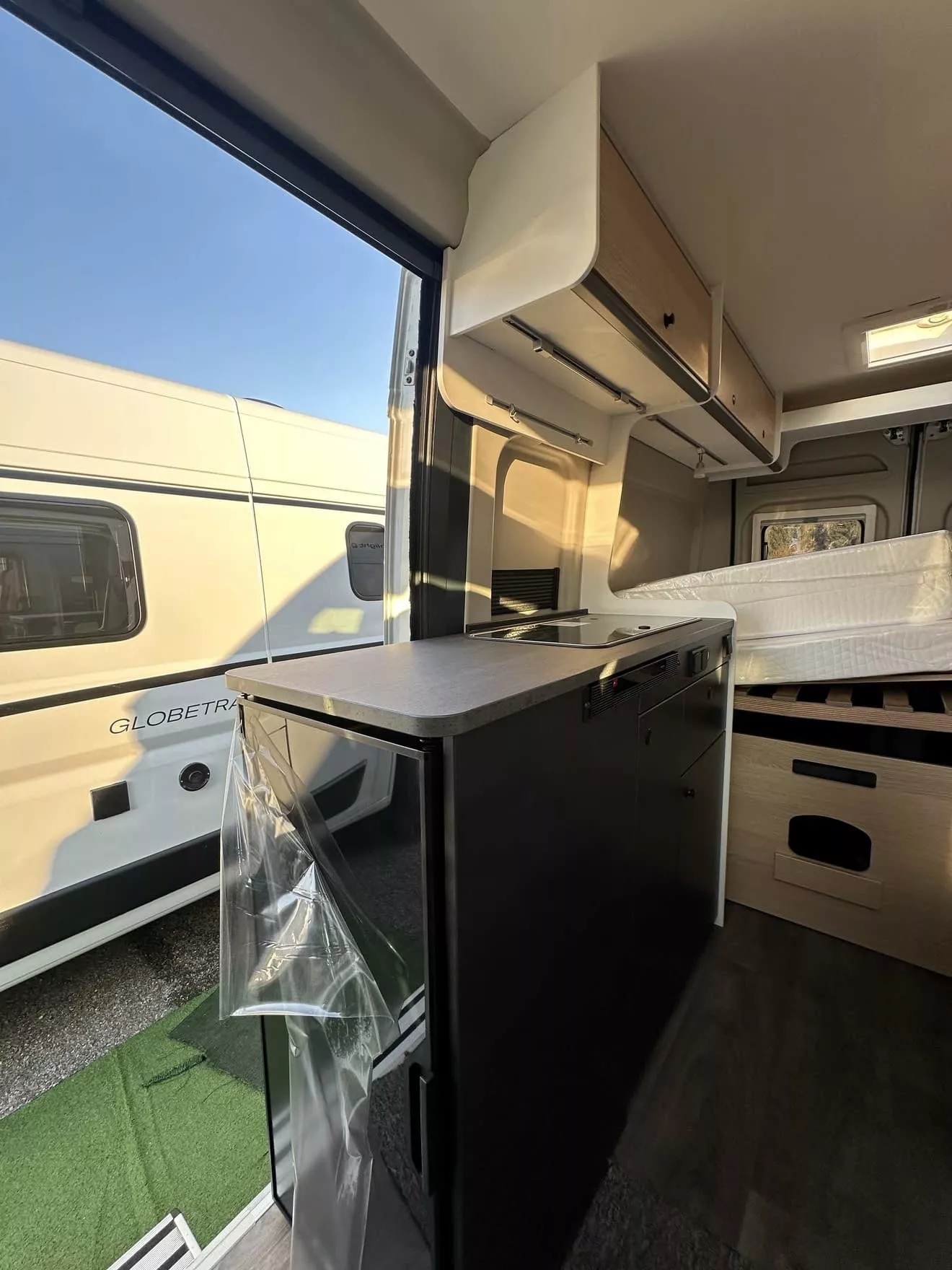 Intérieur d'un camping-car moderne avec cuisine et lit, vue sur l'extérieur ensoleillé