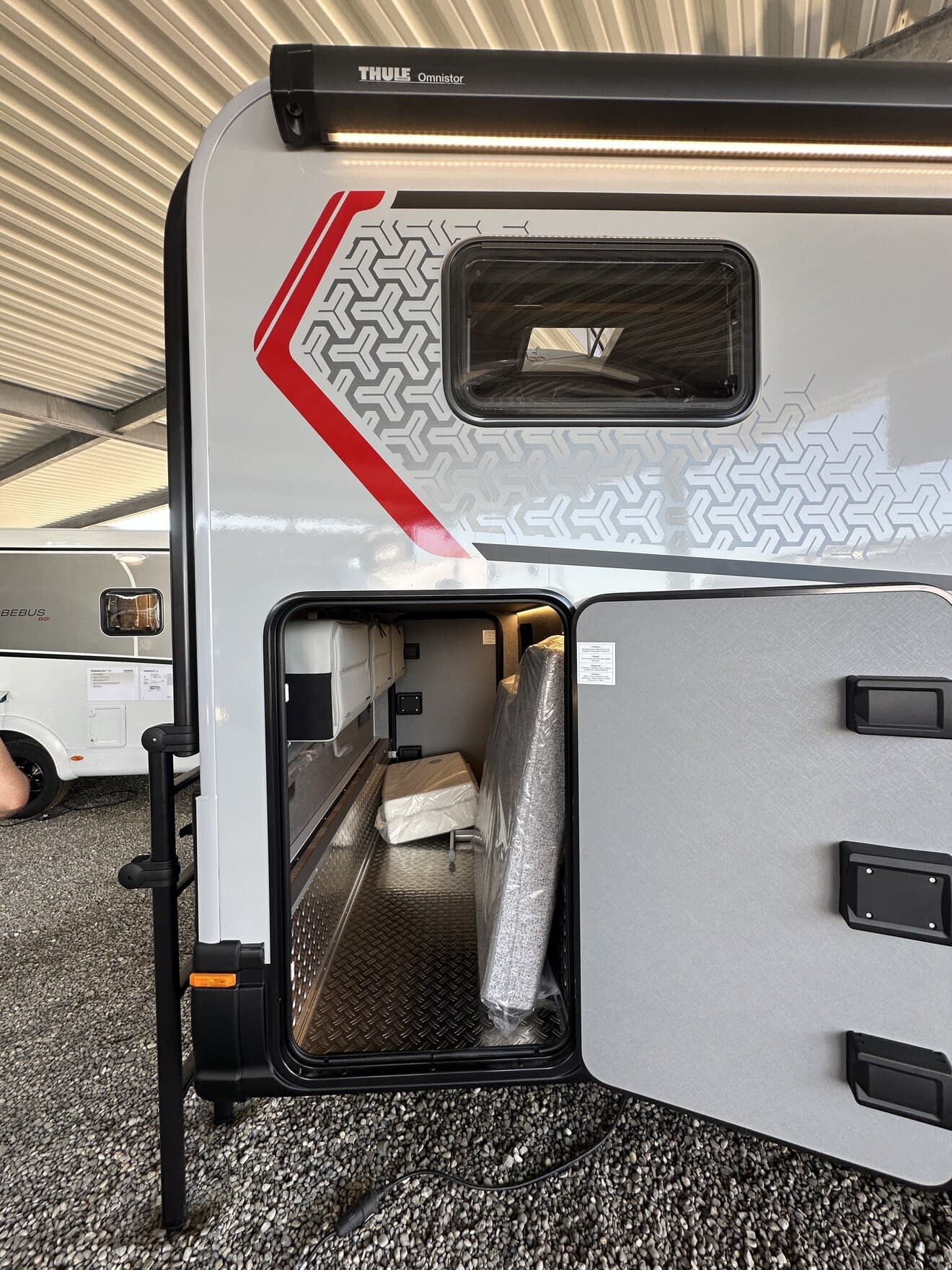 Compartiment de rangement ouvert d'une caravane sous abri, avec matelas emballé à l'intérieur.