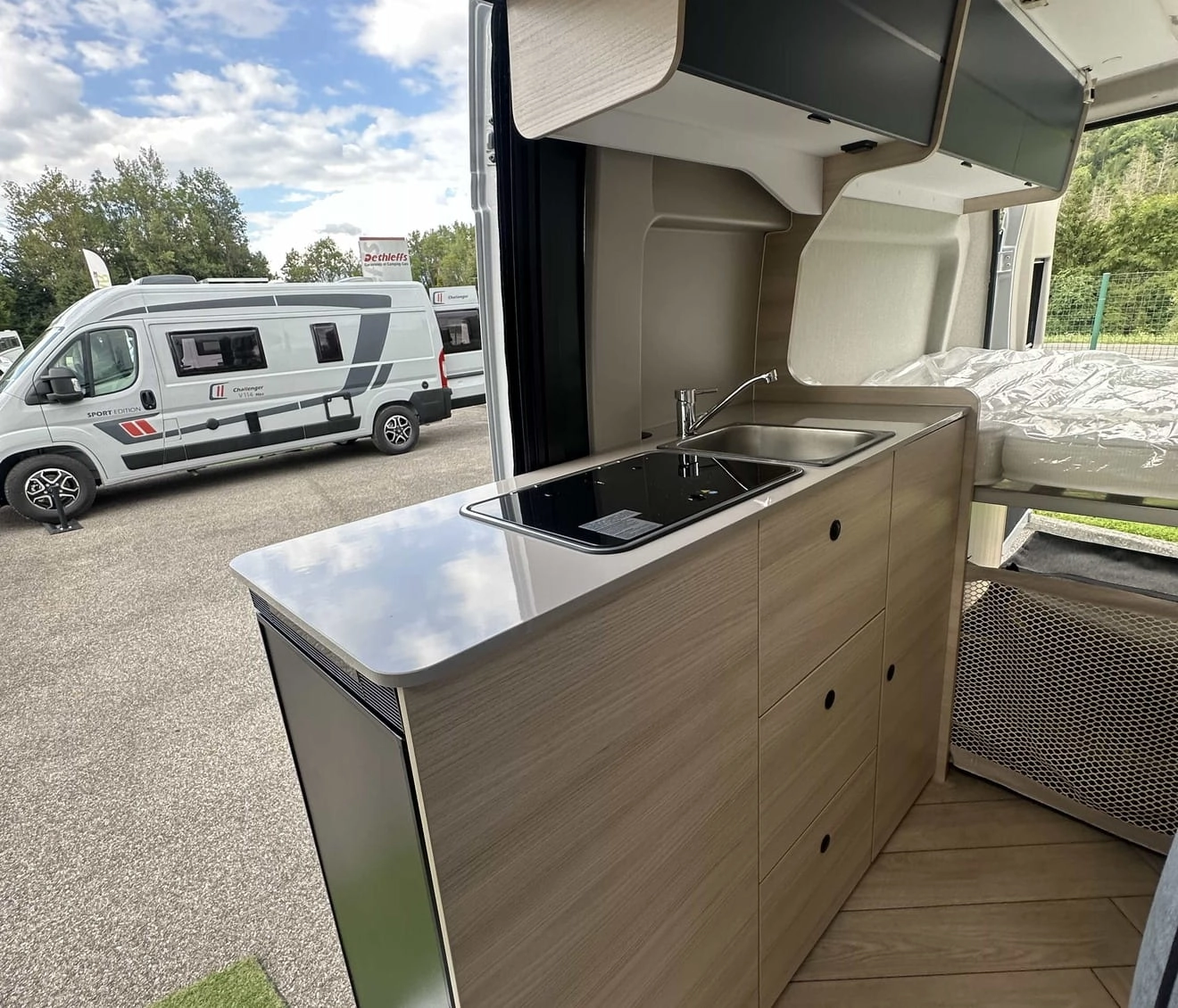 Intérieur d'un camping-car moderne avec cuisine équipée et lit, vue sur l'extérieur.