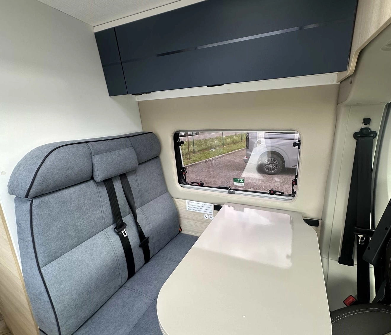 Intérieur d'un camping-car avec banquette et table pliante, vue sur fenêtre latérale.