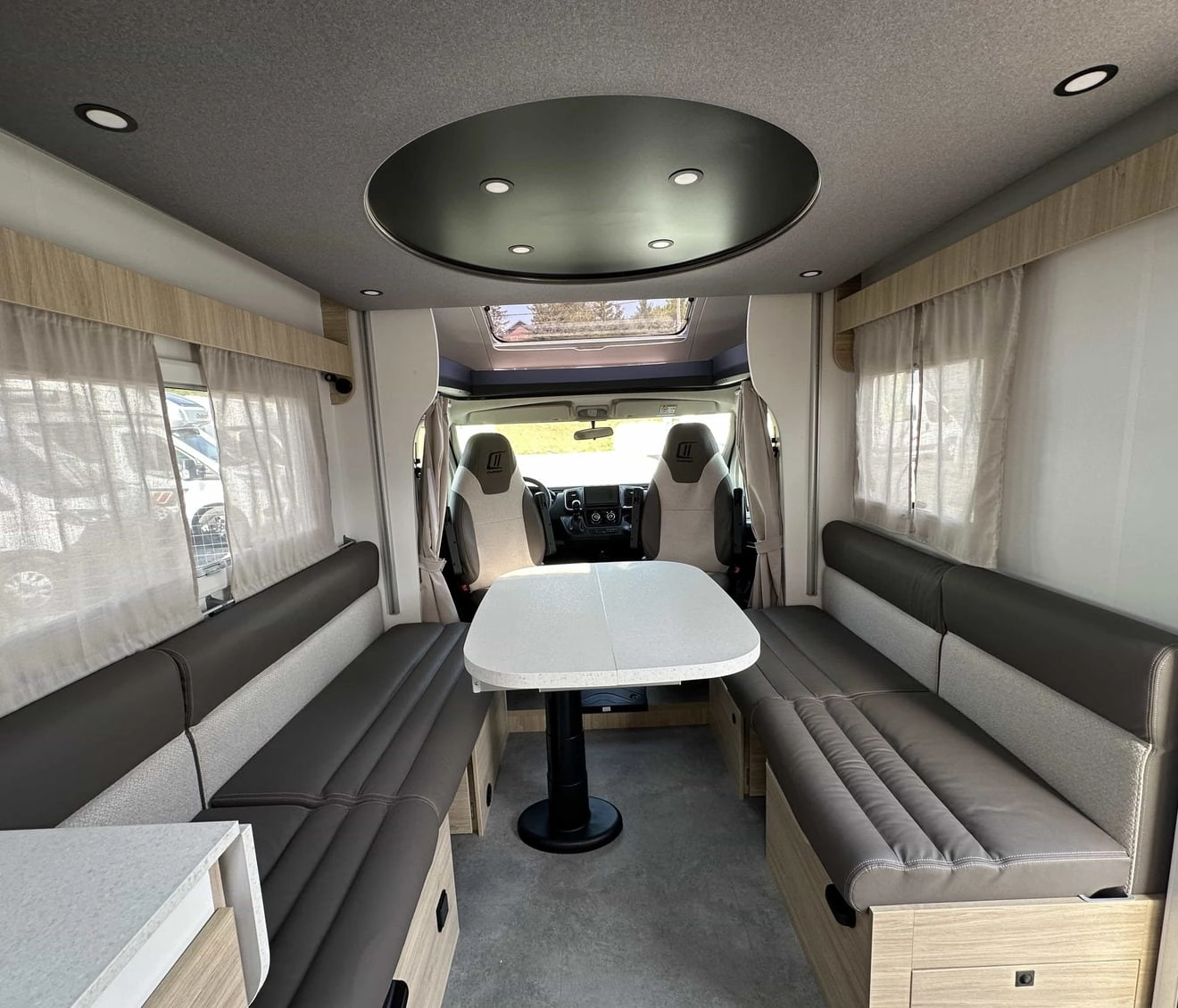 Intérieur spacieux d'un camping-car moderne avec banquettes et table centrale.