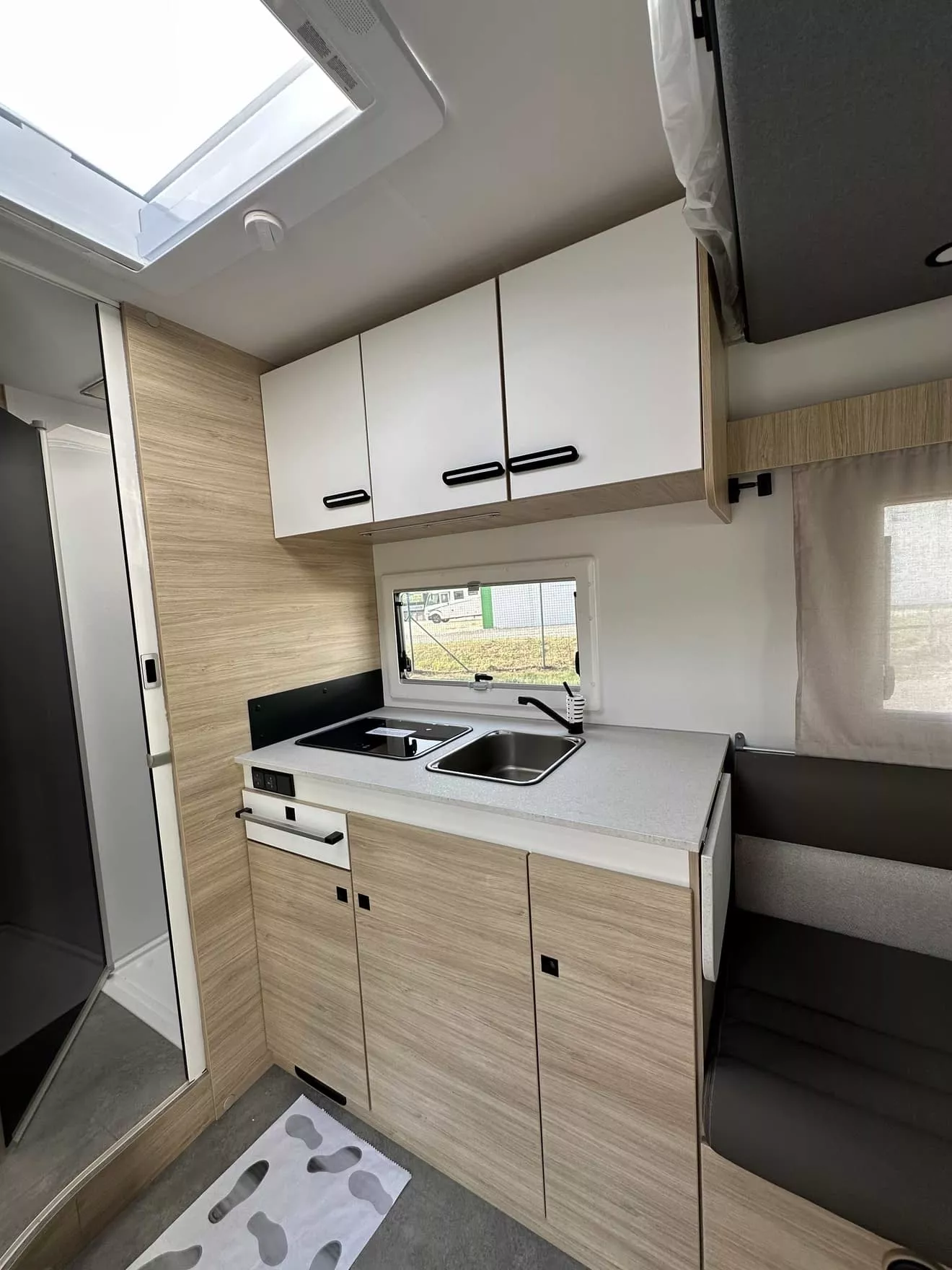 Cuisine moderne de camping-car avec évier, plaques de cuisson et rangements en bois clair.