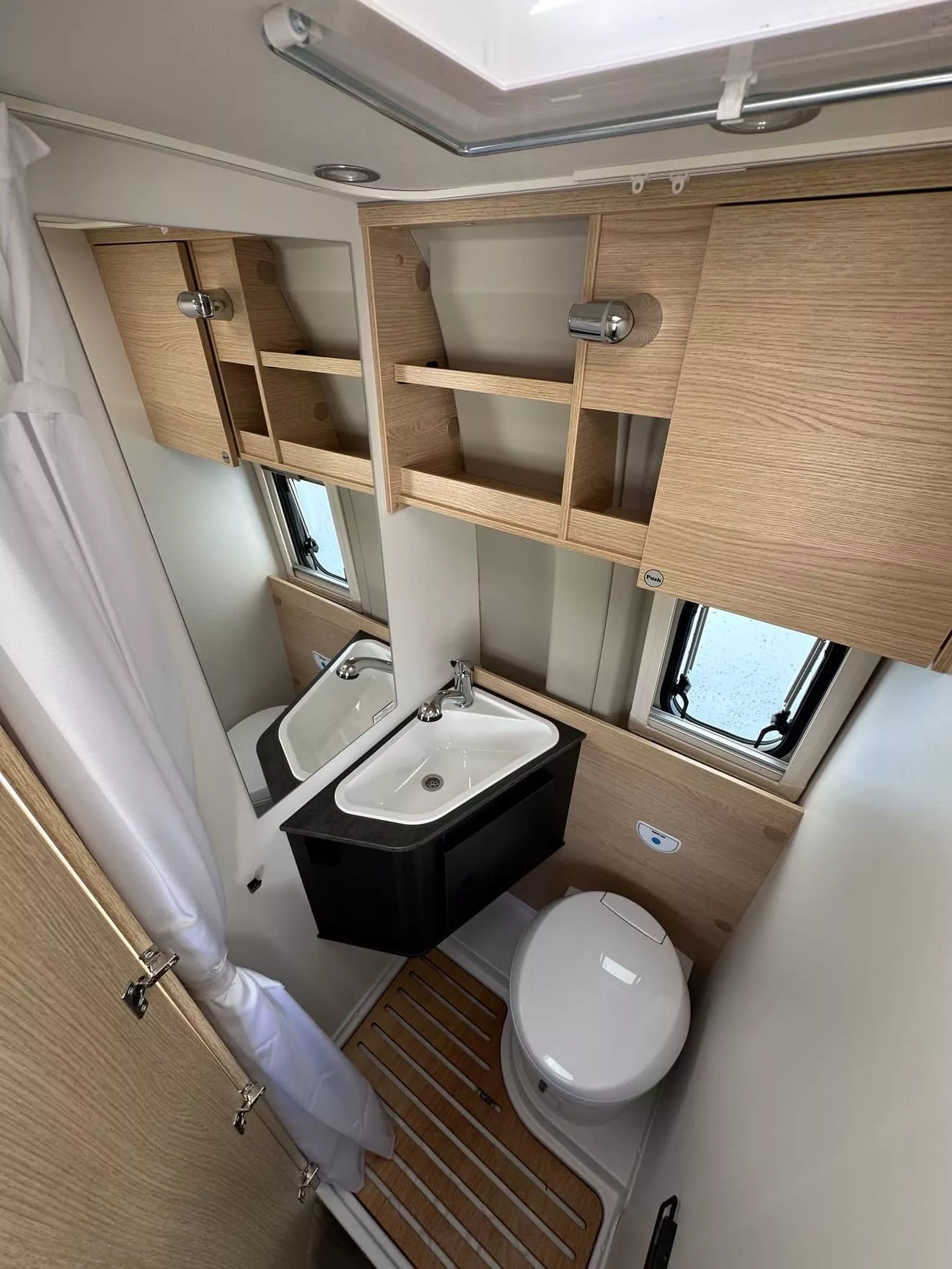 Salle de bain compacte avec lavabo, toilettes et rangements en bois clair dans un camping-car.
