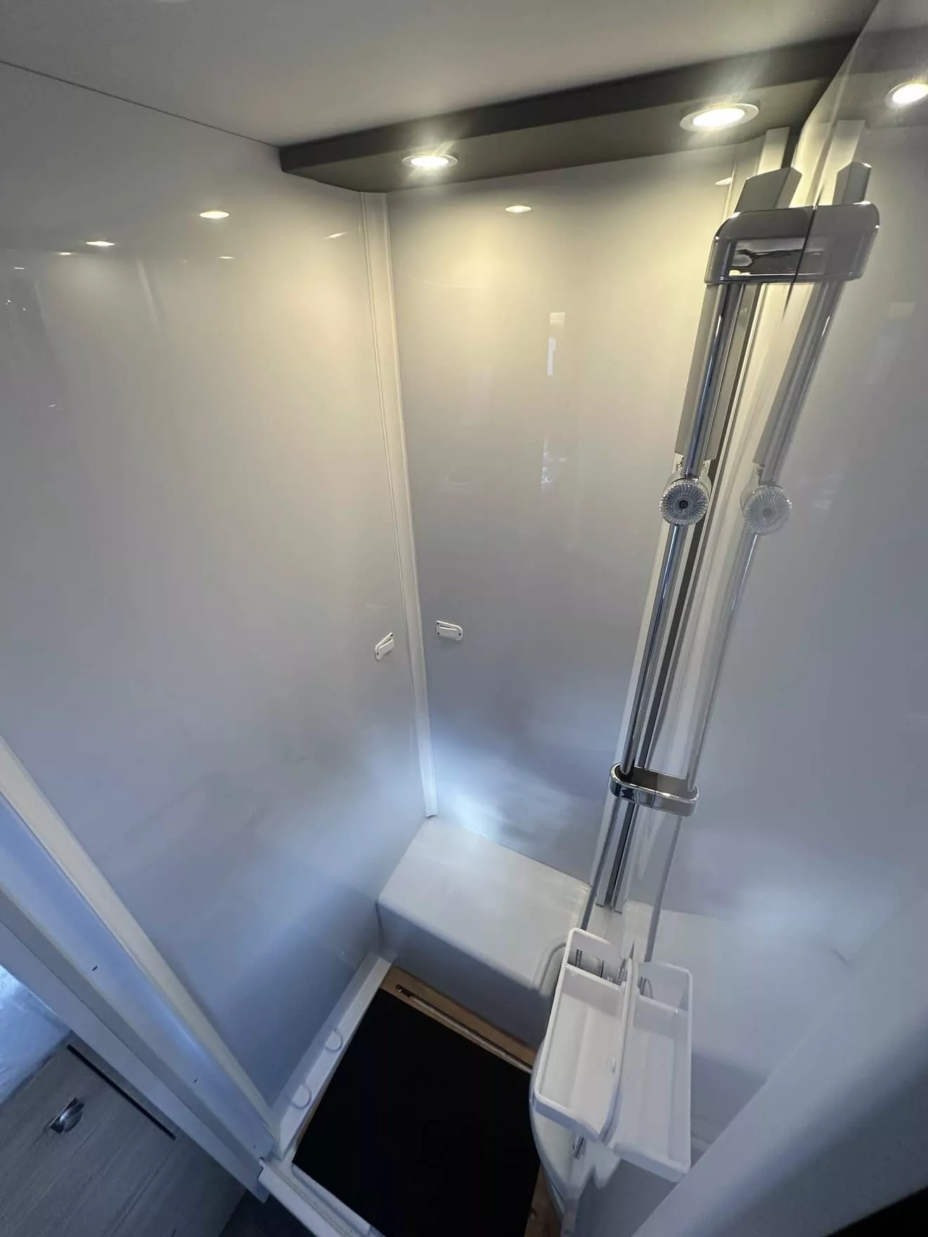 Douche moderne avec parois blanches et éclairage intégré, équipée d'une colonne de douche chromée.