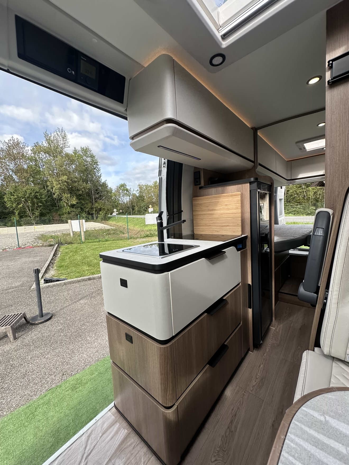 Intérieur moderne d'un camping-car avec cuisine équipée et vue sur l'extérieur verdoyant.