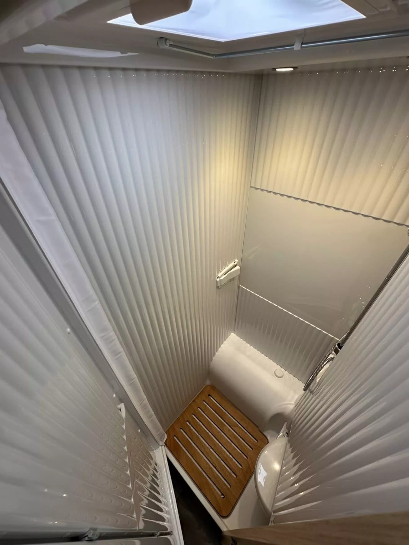 Douche compacte avec parois blanches et sol en bois, éclairage intégré, vue depuis le haut.