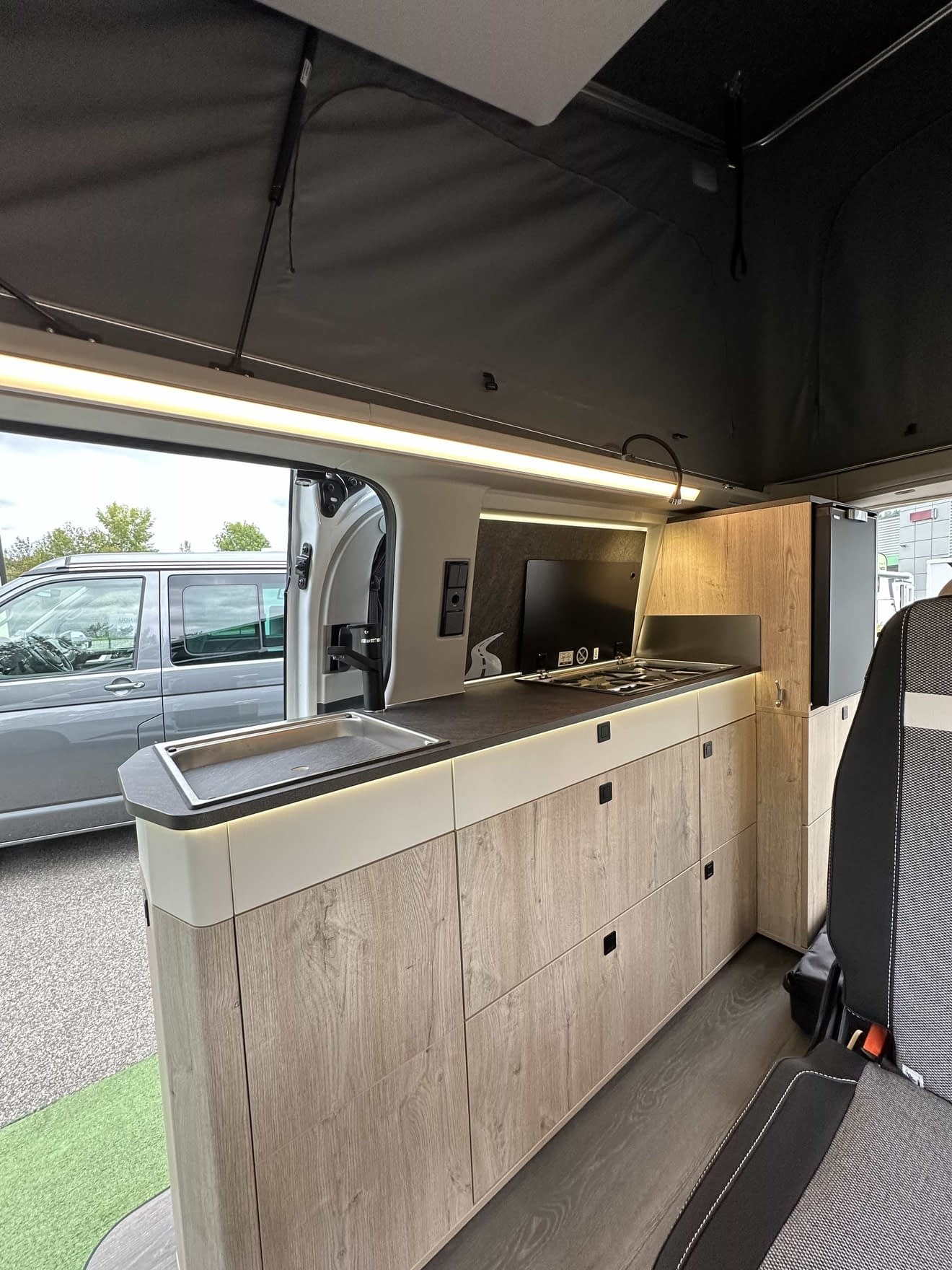 Intérieur d'un van aménagé avec cuisine moderne et espace de rangement en bois clair.