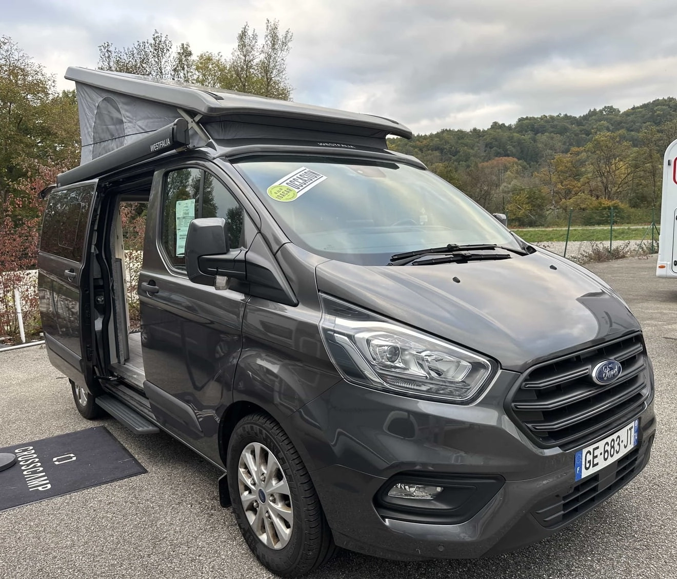 Van aménagé Ford avec toit relevable sur un parking, modèle Westfalia.