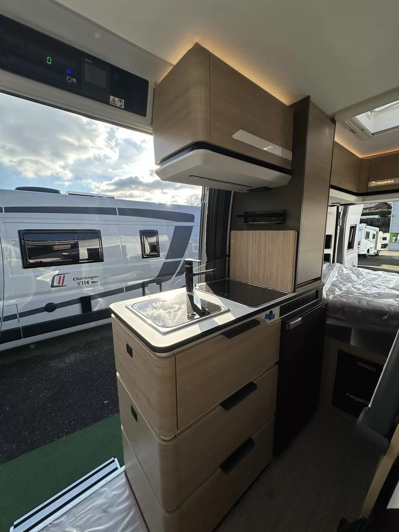 Intérieur d'un camping-car moderne avec cuisine équipée et vue sur un autre véhicule stationné.