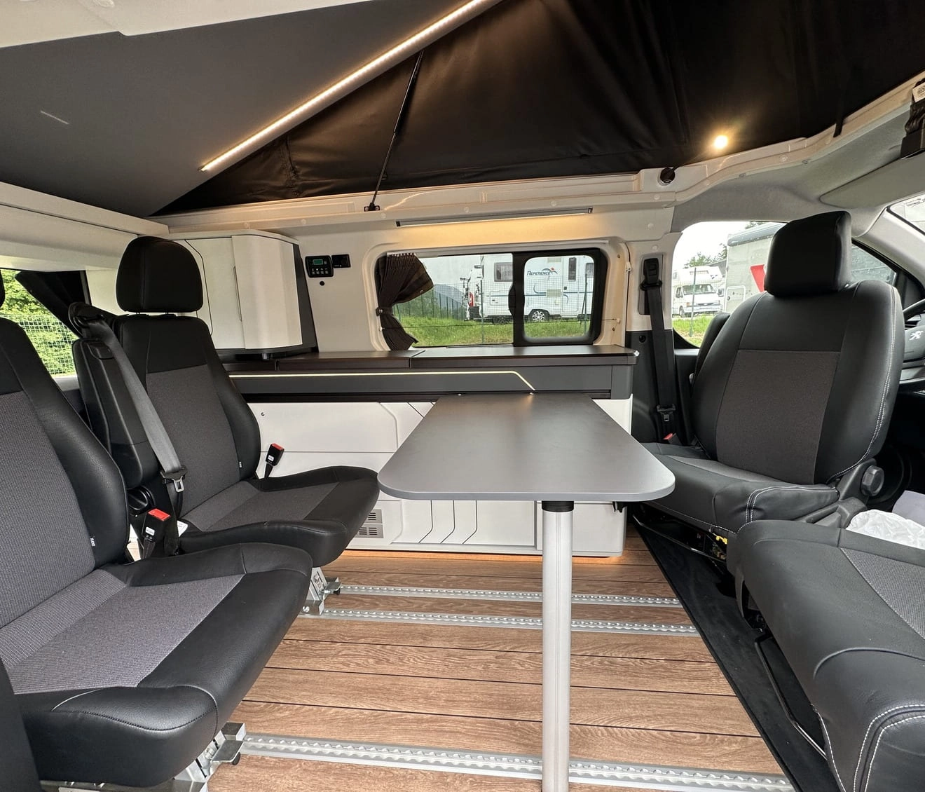 Intérieur d'un van aménagé avec sièges et table, sol en bois