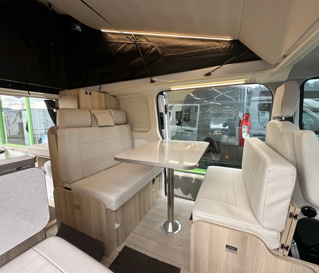 Intérieur d'un van aménagé avec sièges et table en bois clair, éclairage LED
