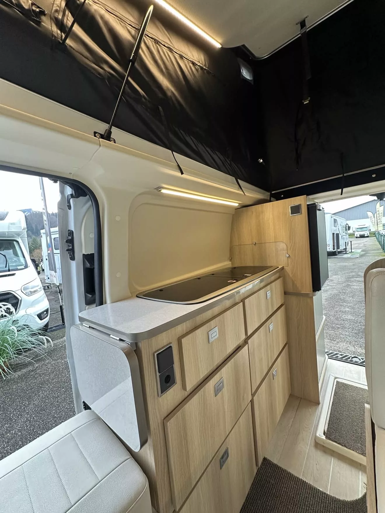 Intérieur d'un van aménagé avec cuisine en bois clair et éclairage LED.