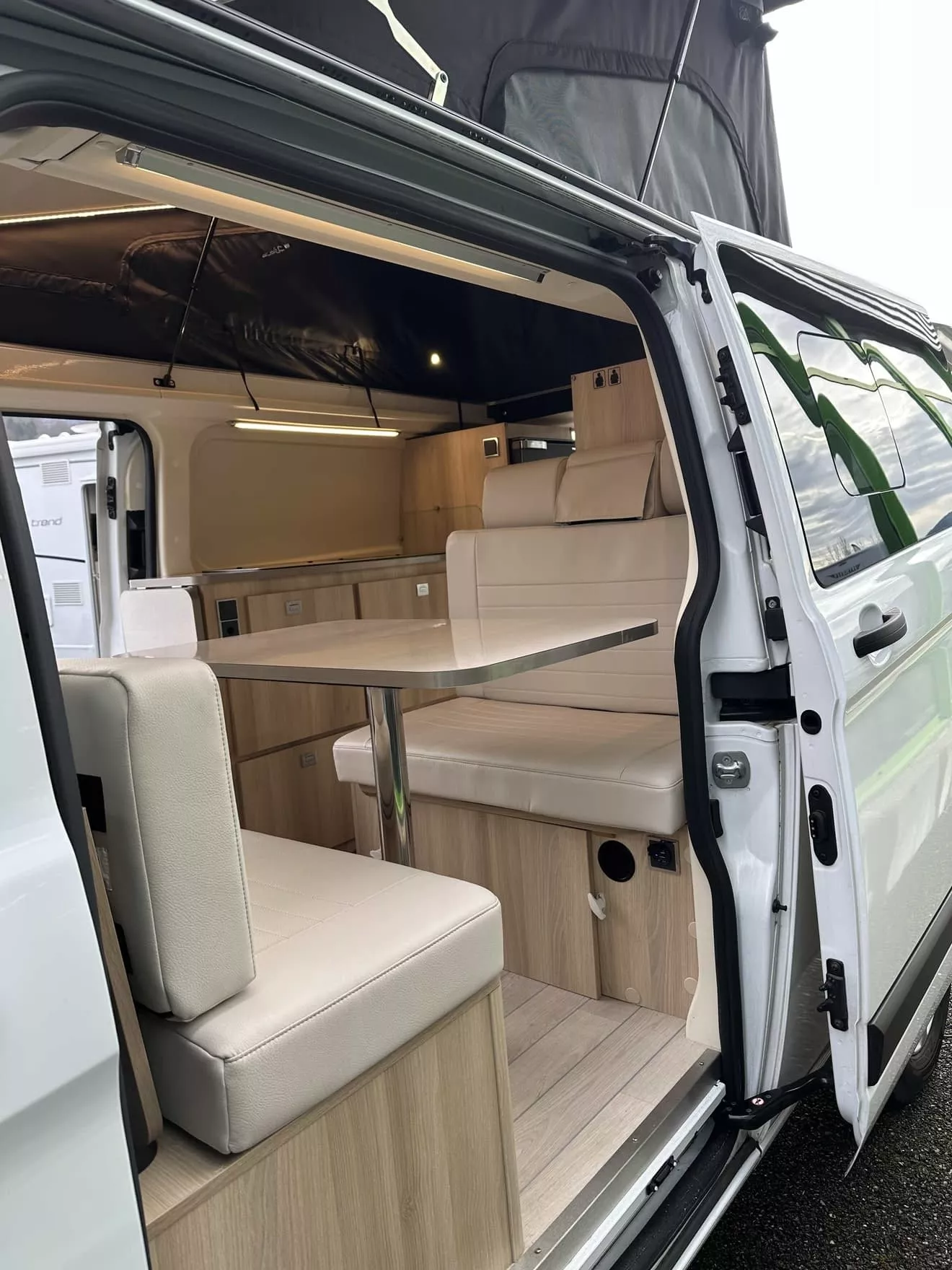 Intérieur d'un van aménagé avec table et banquettes en bois clair.