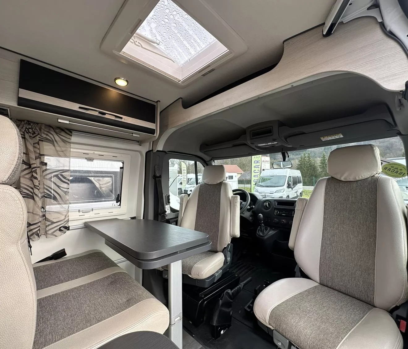 Intérieur d'un camping-car moderne avec sièges et table, vue sur l'extérieur.