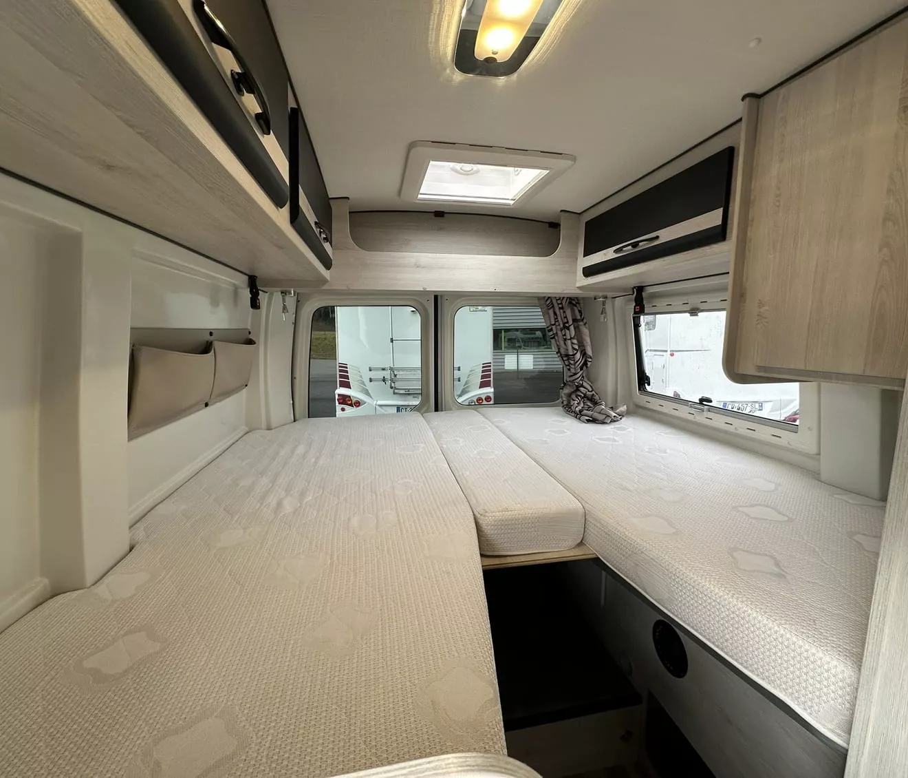 Intérieur d'un camping-car avec lits jumeaux et rangements en bois clair.