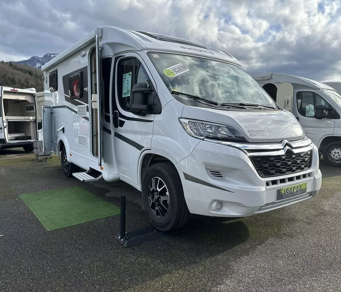Camping-car Citroën blanc stationné sur un parking, ciel nuageux en arrière-plan.