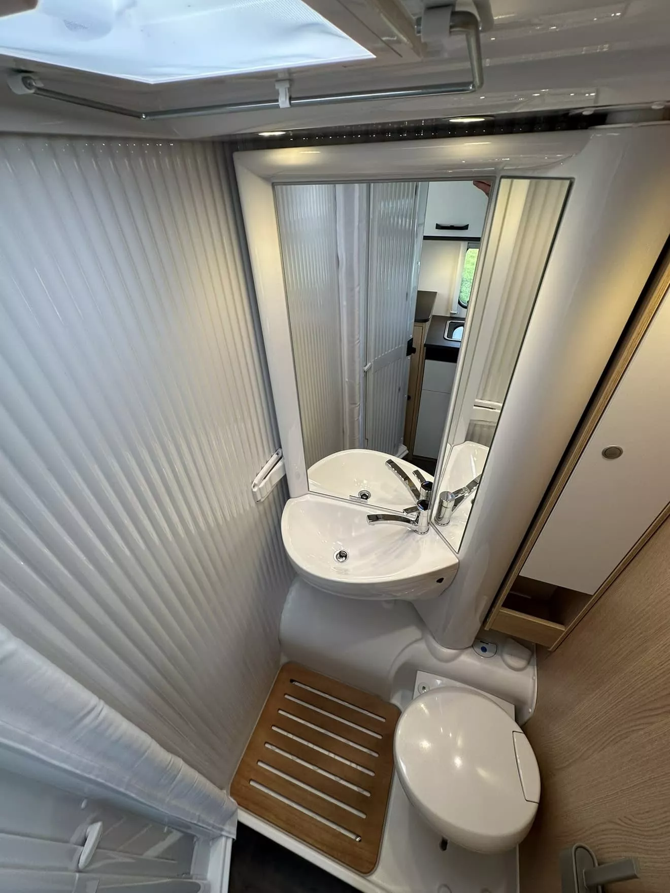Salle de bain compacte avec lavabo, miroir et toilettes dans un camping-car moderne.