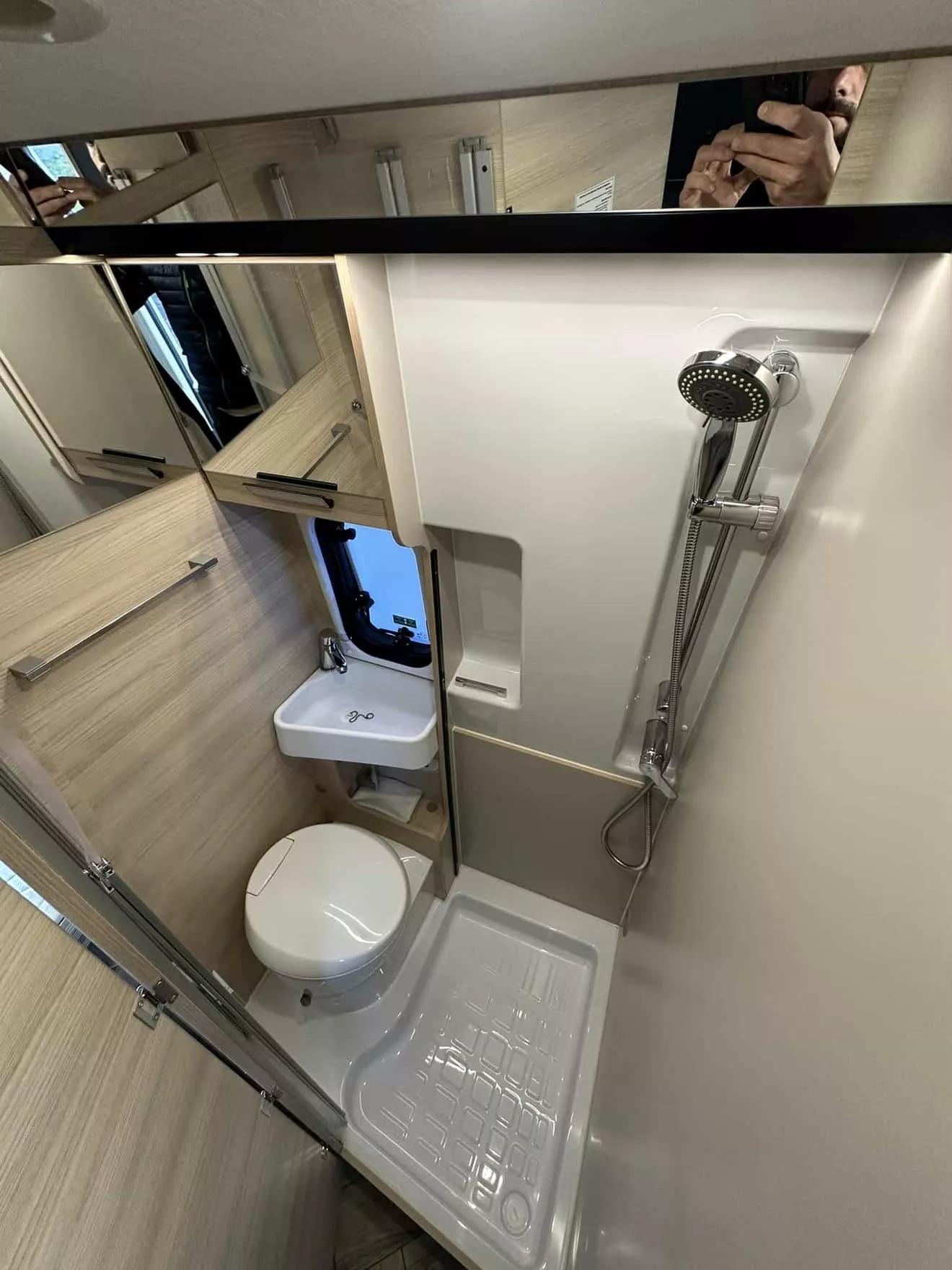 Salle de bain compacte avec douche, lavabo et toilettes dans un camping-car moderne.