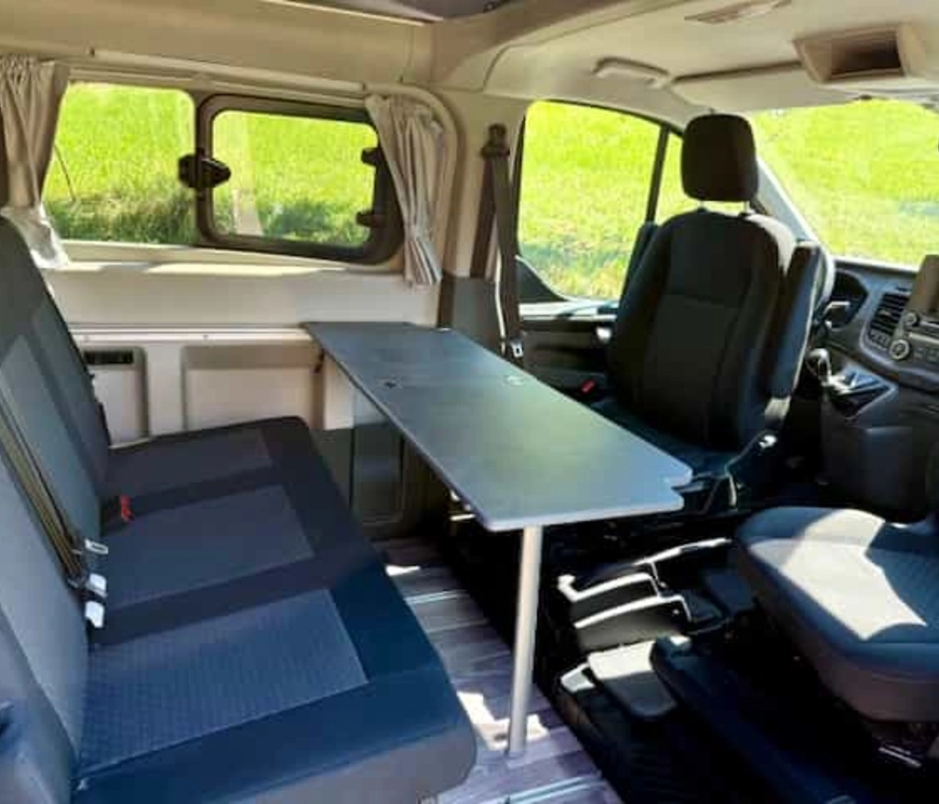 Intérieur d'un van aménagé avec sièges et table pliante, vue sur l'extérieur verdoyant.