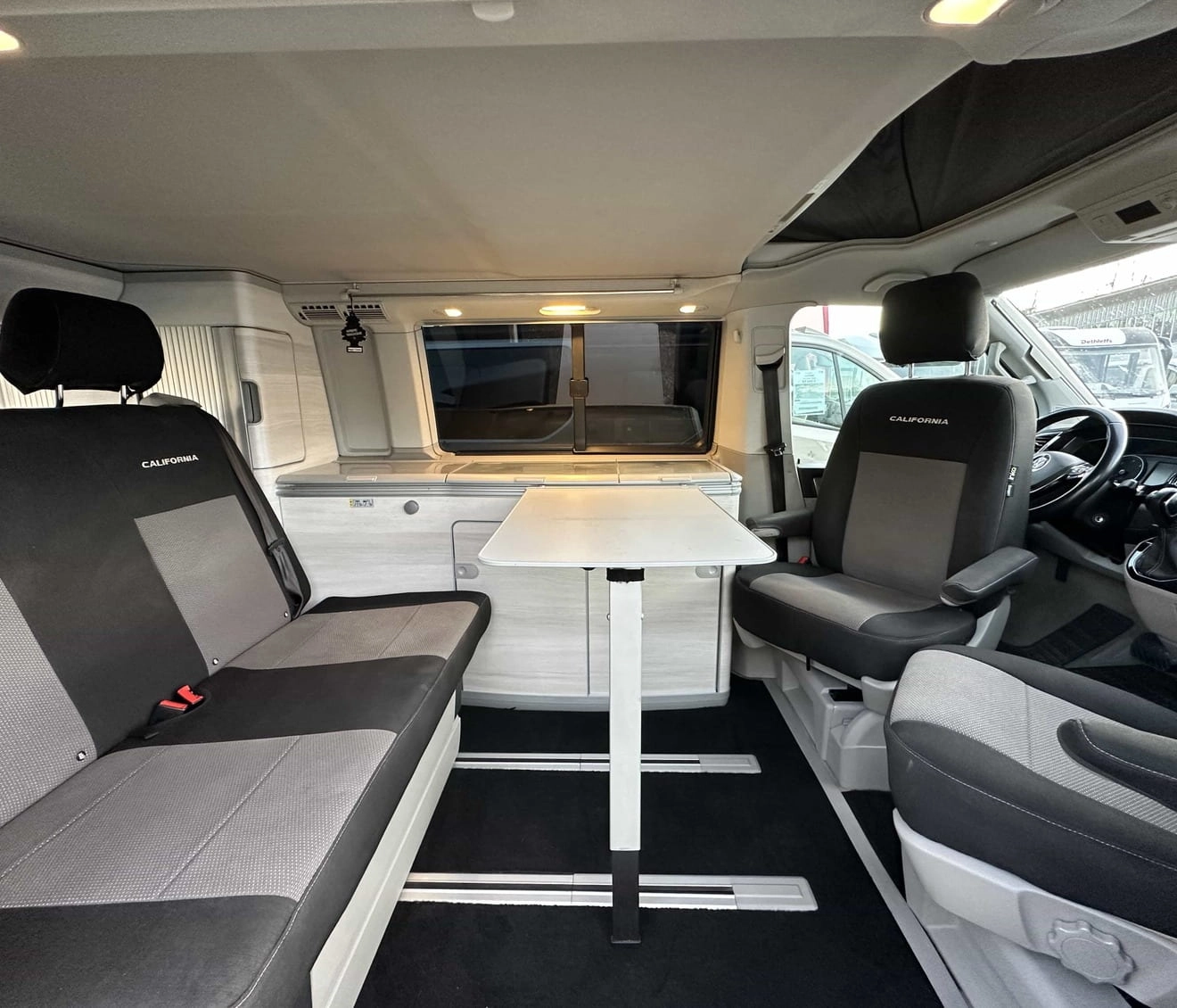 Intérieur d'un van aménagé avec sièges et table pliante, modèle California.