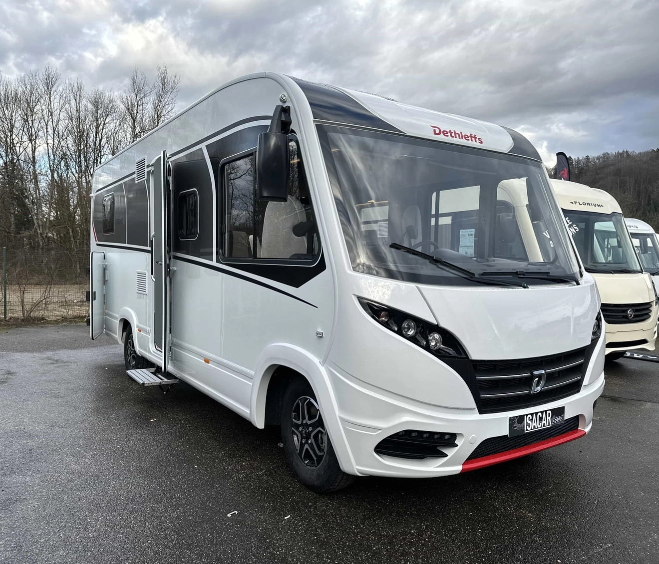 Camping-car Dethleffs blanc stationné sur un parking, ciel nuageux en arrière-plan.