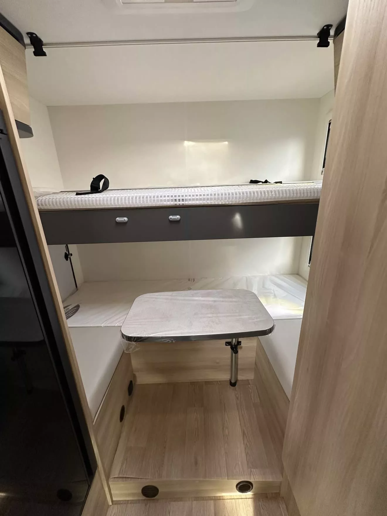 Intérieur d'un camping-car avec lits superposés et table pliante en bois clair.