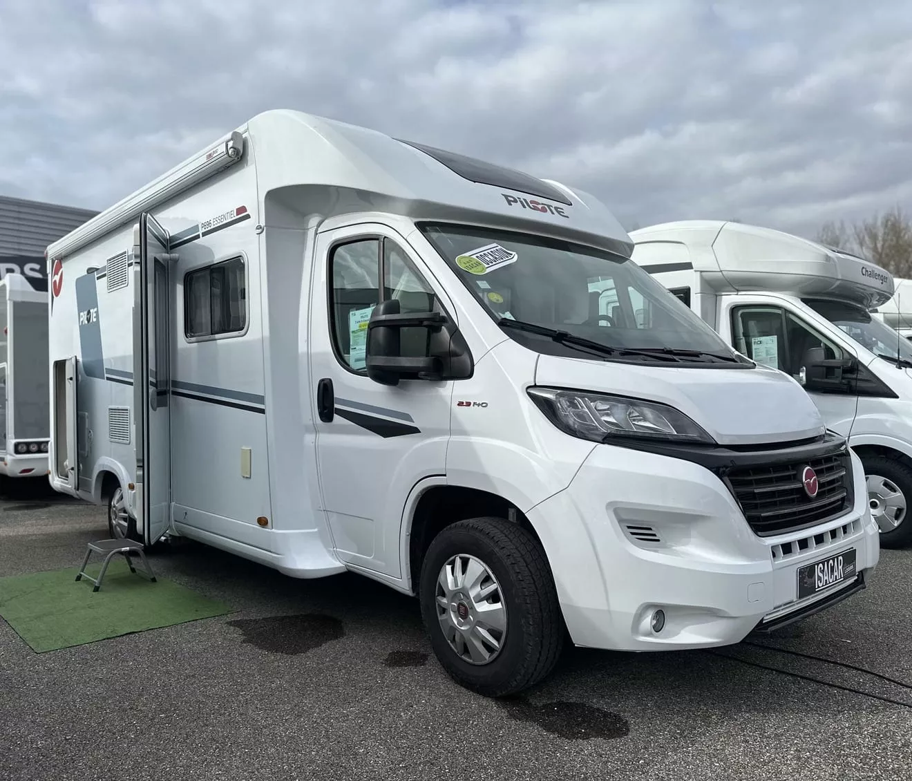 Camping-car blanc stationné sur un parking, modèle Pilote, ciel nuageux en arrière-plan.