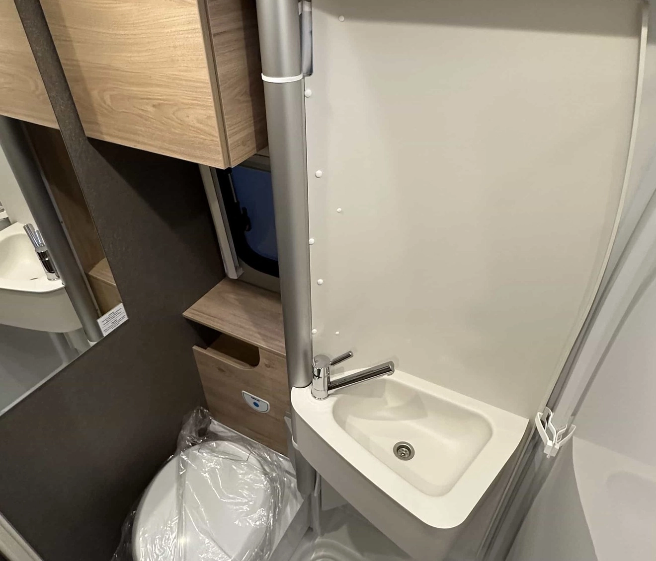 Salle de bain compacte avec lavabo, toilettes et douche dans un camping-car moderne.