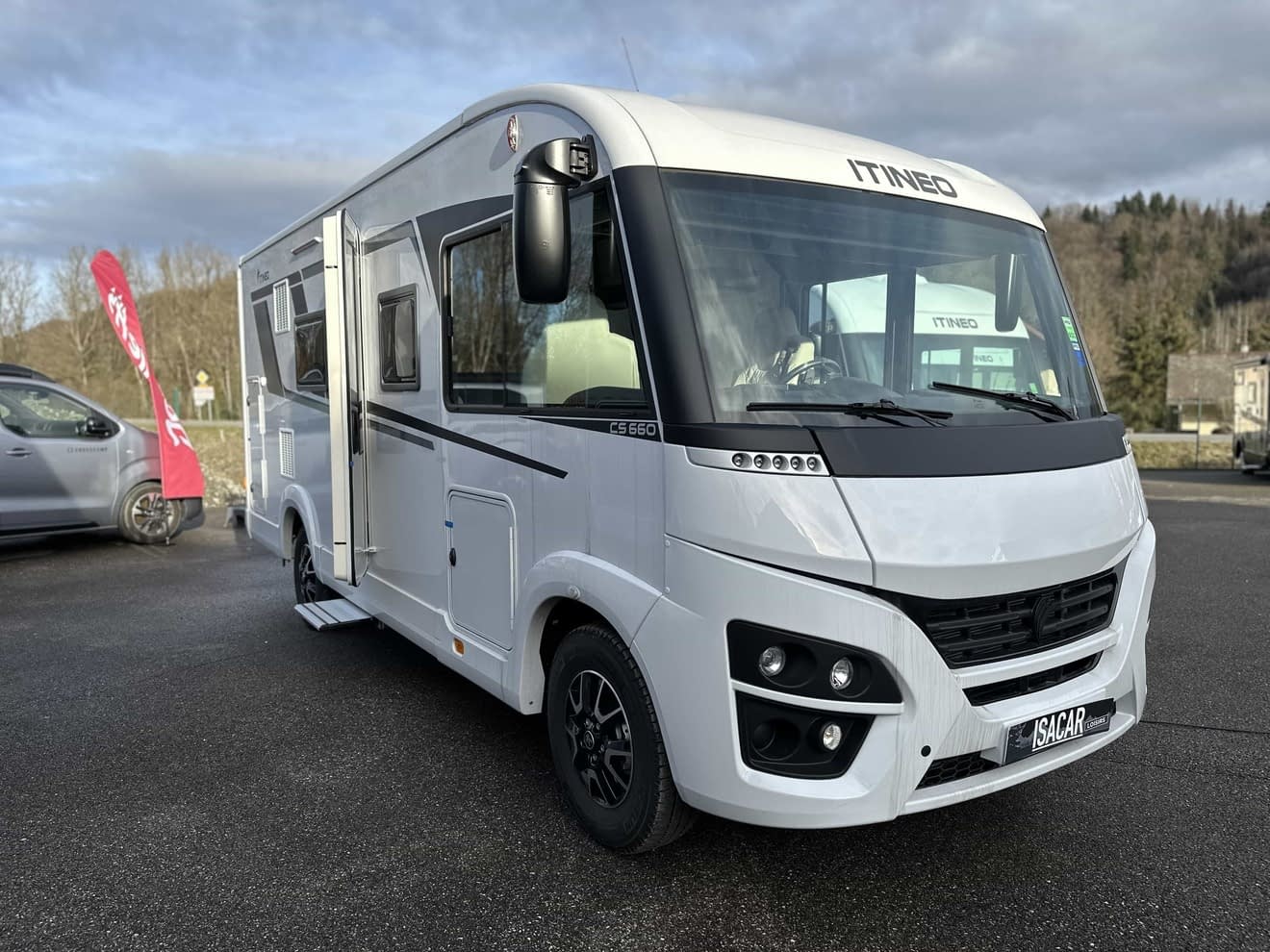 Camping-car Itineo blanc stationné sur un parking, ciel nuageux en arrière-plan.