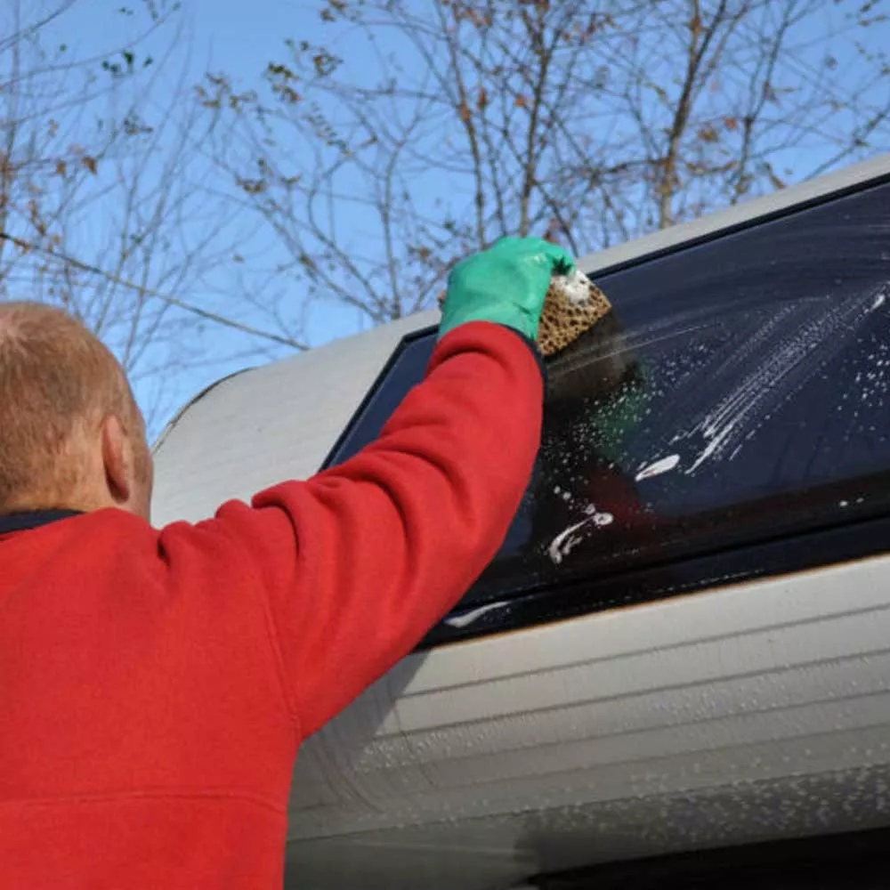 Nettoyage d'une fenêtre de caravane avec une éponge et des gants
