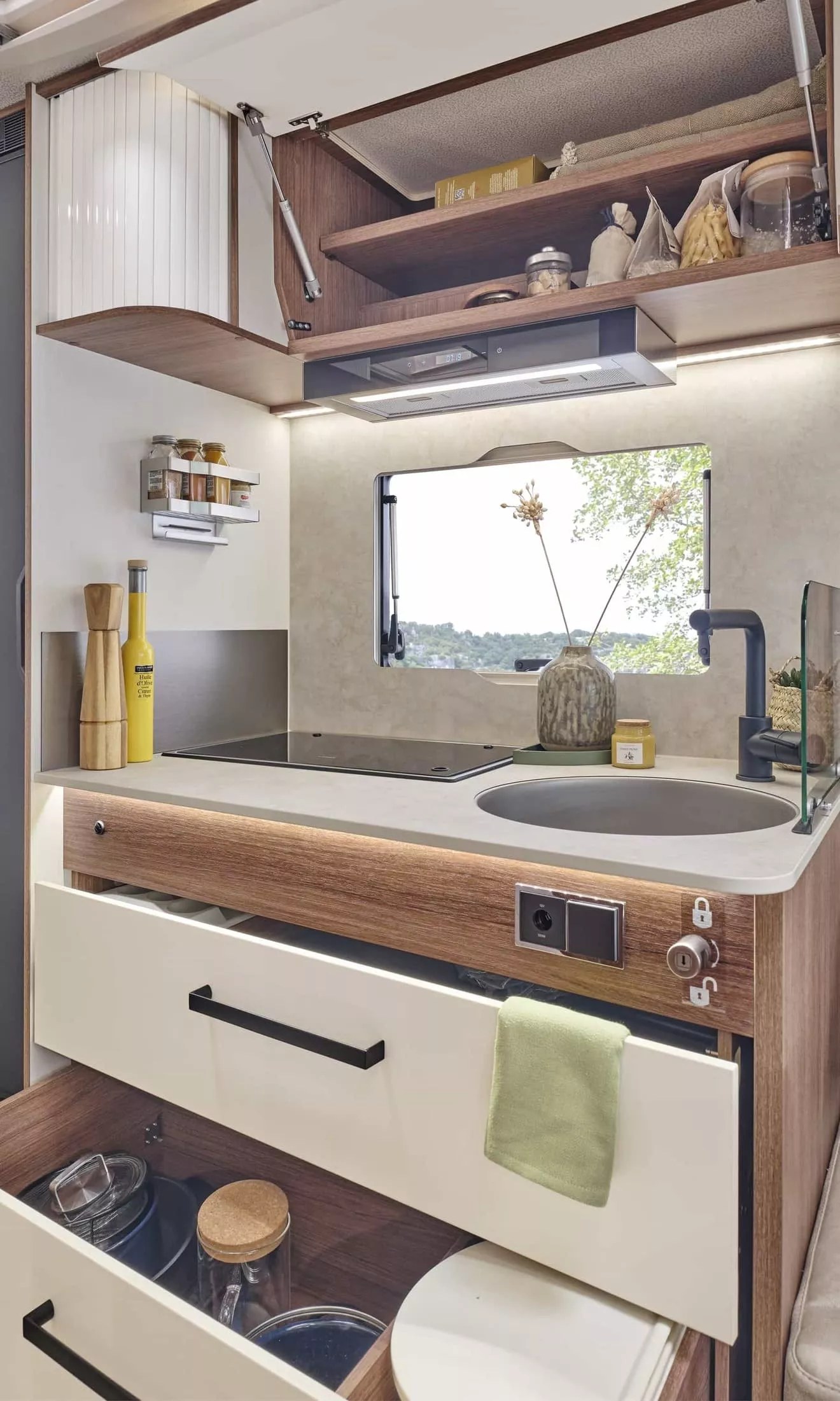 Cuisine compacte de camping-car avec évier, plaques de cuisson et rangements ouverts.