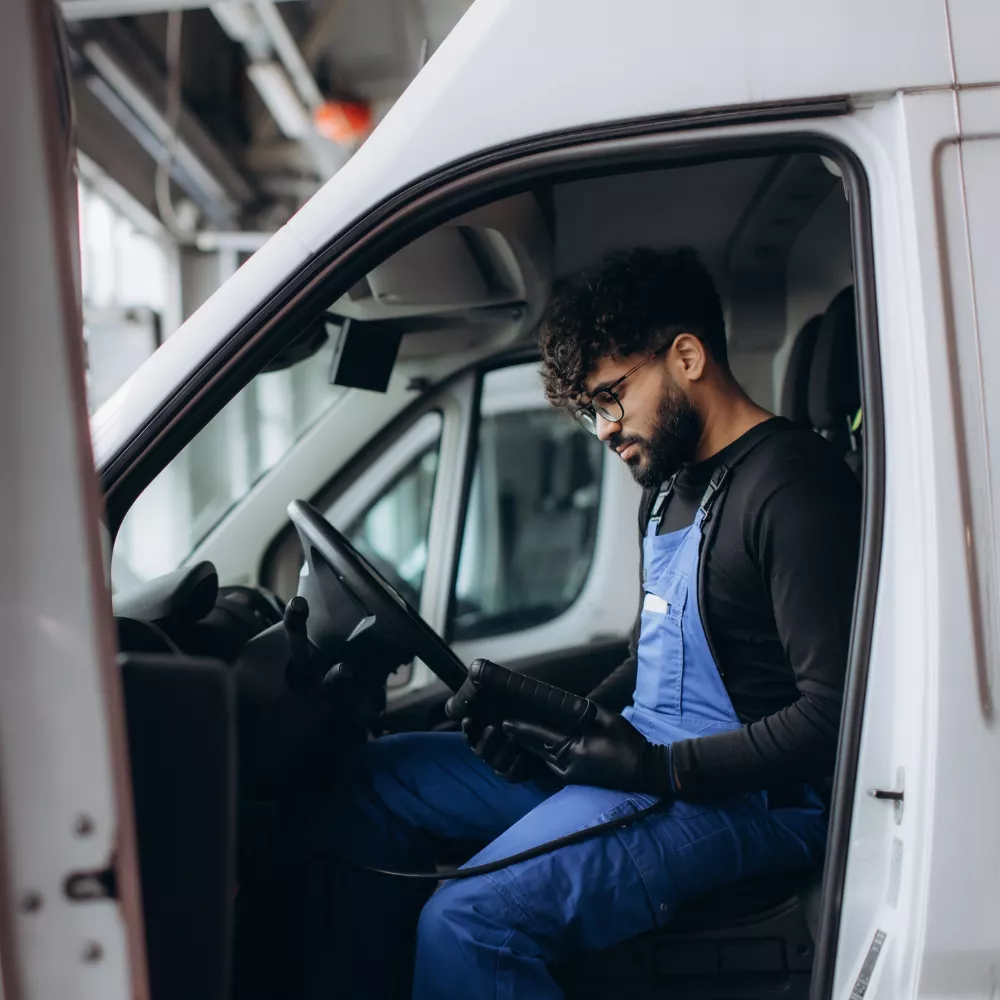 Technicien en bleu de travail dans un véhicule utilitaire, vérifiant un appareil électronique.