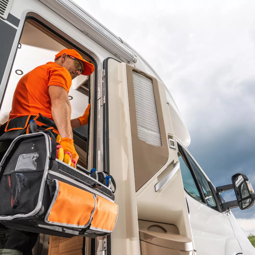 Technicien en uniforme orange inspectant un camping-car avec une trousse à outils