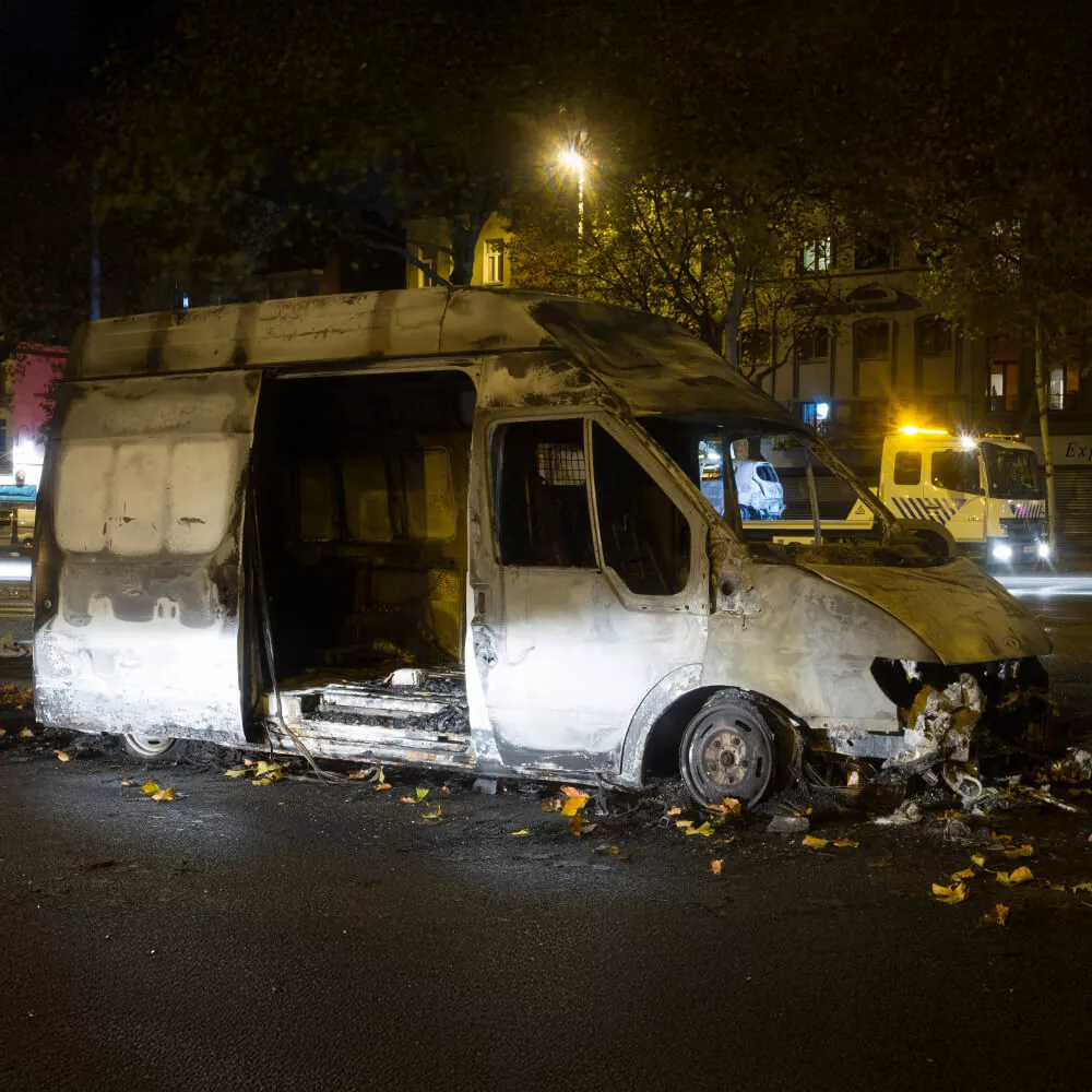 Fourgon incendié sur une route la nuit, avec dépanneuse en arrière-plan
