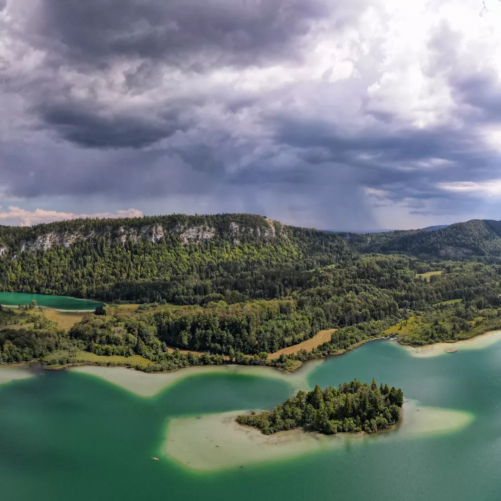 Paysage de lac entouré de forêts sous un ciel nuageux, région montagneuse.