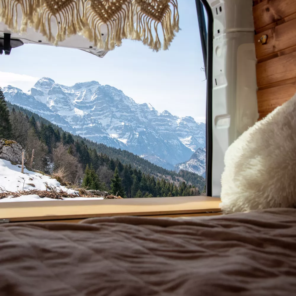 Vue montagne depuis l'intérieur d'un van aménagé, avec lit et coussin